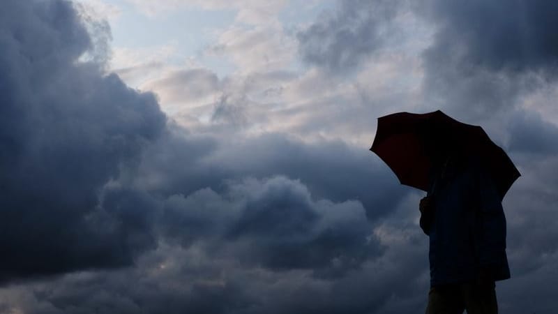 Ein Mann mit Schirm vor grauen Wolken: Am Donnerstag drohen in Teilen Deutschlands schwere Unwetter.