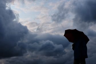 Ein Mann mit Schirm vor grauen Wolken: Am Donnerstag drohen in Teilen Deutschlands schwere Unwetter.