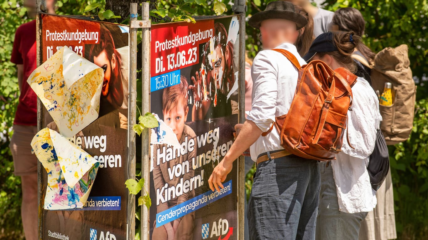 Passanten zerreißen ein Plakat der AfD, mit dem zum Protest gegen die Drag-Lesung in München aufgerufen wird. Die Veranstaltung für Kinder findet am Dienstag in einer Bibliothek statt.