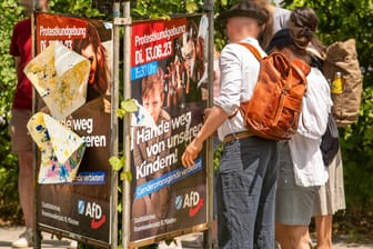 Passanten zerreißen ein Plakat der AfD, mit dem zum Protest gegen die Drag-Lesung in München aufgerufen wird. Die Veranstaltung für Kinder findet am Dienstag in einer Bibliothek statt.