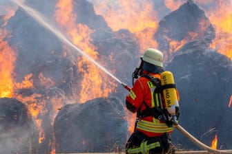 Symbolbild eines Feuerwehrmannes, der ein Feuer löscht: droht uns das bald auch in Deutschland durch den Klimawandel?