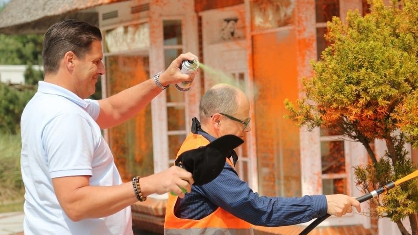 Klimaaktivist auf Sylt: Ein Anwohner sprüht den Mann an, während der orange Farbe auf ein Gebäude spritzt.