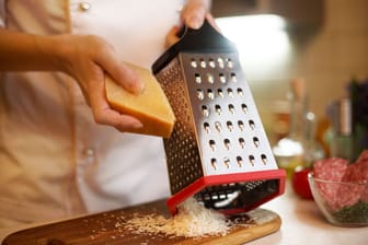 Ein Koch reibt Käse: Die Küchenreibe hat vier unterschiedlich strukturierte Seiten.