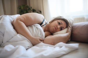 Übergewichtige Frau liegt traurig im Bett