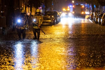 Duisburg: Feuerwehrleute suchen auf einer überfluteten Straße nach Gullydeckeln.
