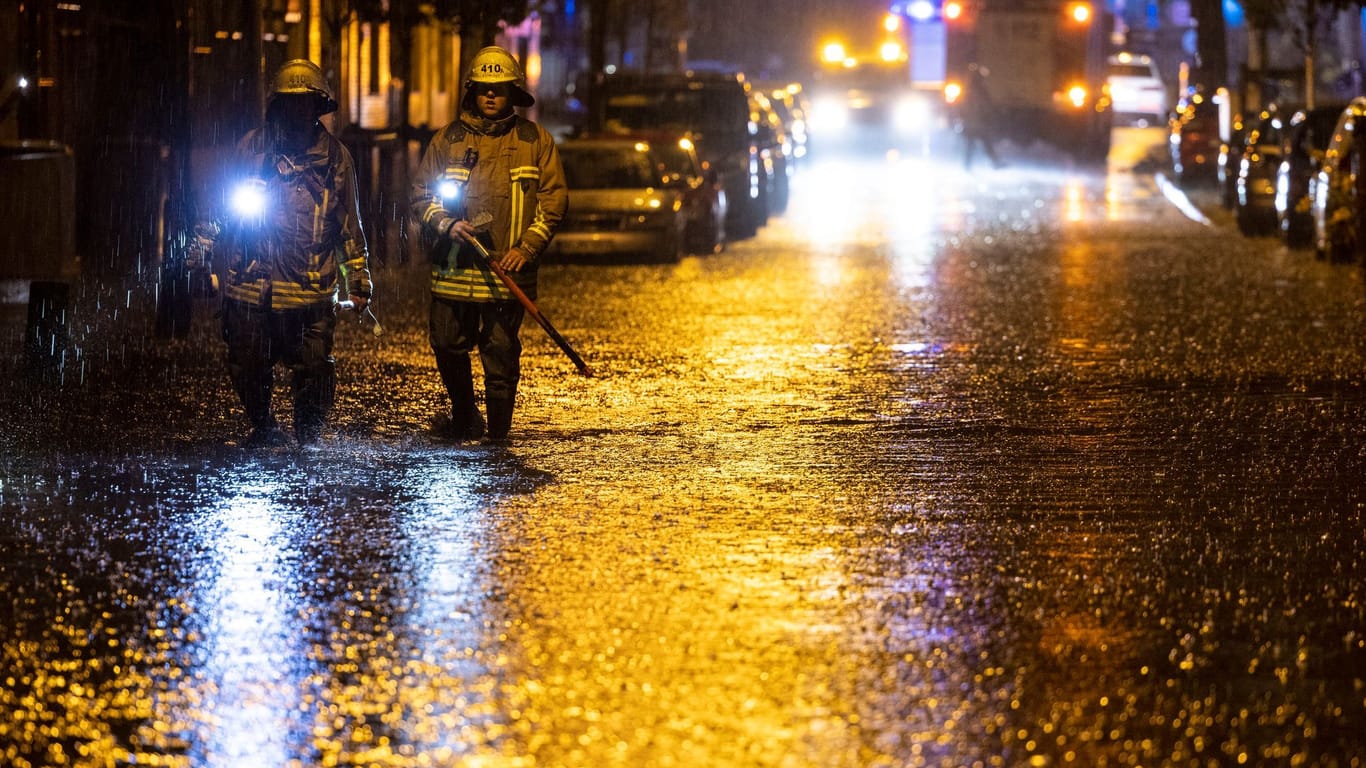 Duisburg: Feuerwehrleute suchen auf einer überfluteten Straße nach Gullydeckeln.