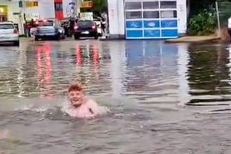 Ein junger Mann schwimmt in Braunschweig auf einer überfluteten Straße