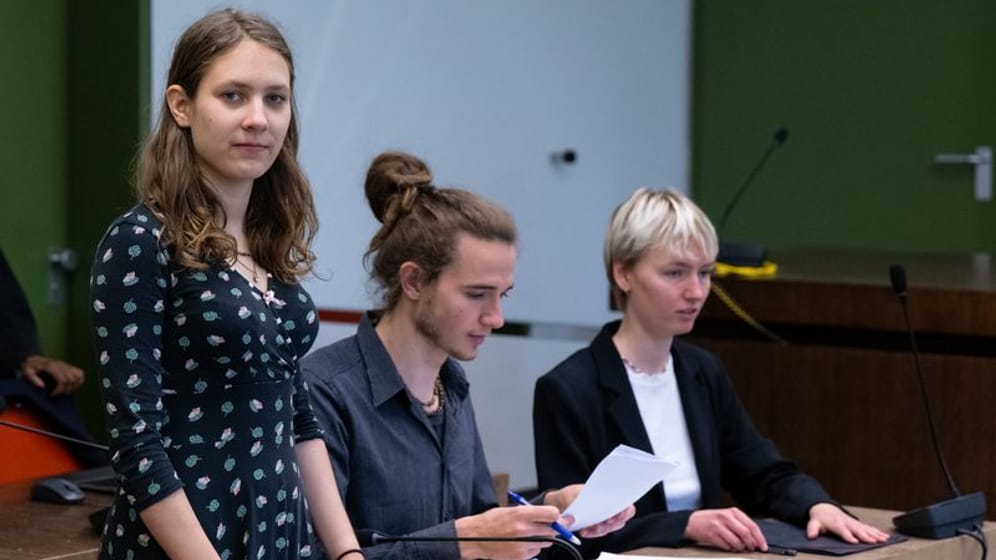 Die drei wegen Hausfriedensbruch angeklagten Klimaaktivisten nehmen vor Prozessbeginn im Verhandlungssaal ihre Plätze ein: Sie störten ein Spiel des FC Bayerns.