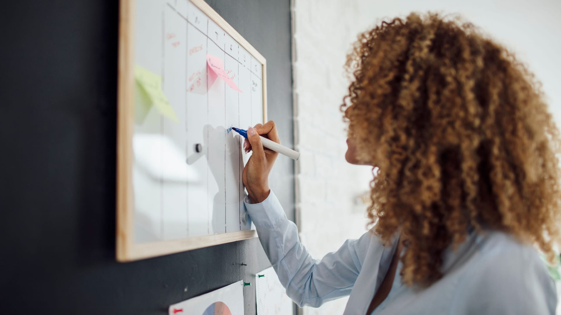 Eine Frau trägt Aufgaben in einen Plan ein: Seinen Arbeitstag zu strukturieren, kann förderlich für die Produktivität sein.