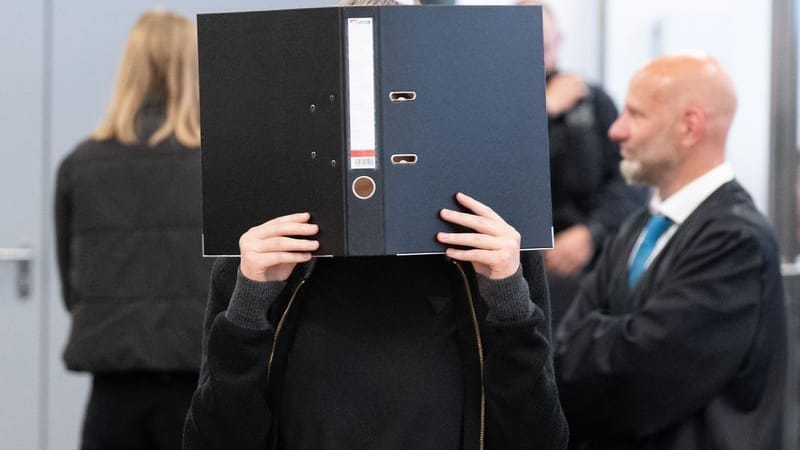 Die Angeklagte Lina E. steht bei der Fortsetzung des Prozesses im Oberlandesgericht (OLG) Dresden im Verhandlungssaal und hält einen Aktenordner vor ihr Gesicht. Die Angeklagte Lina E. steht bei der Fortsetzung des Prozesses im Oberlandesgericht (OLG) Dresden im Verhandlungssaal und hält einen Aktenordner vor ihr Gesicht.