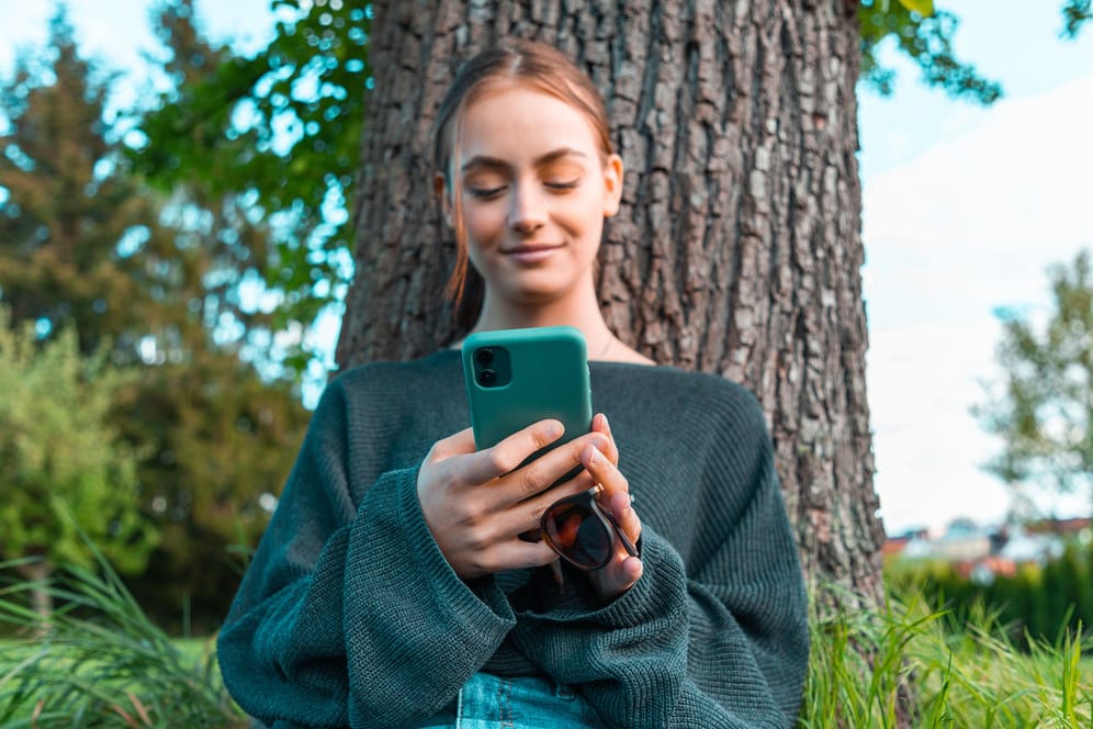 Frau blickt lächelnd auf ihr Smartphone (Symbolbild): Der Online-Händler Amazon plant angeblich den Einstieg in den Mobilfunk-Markt.