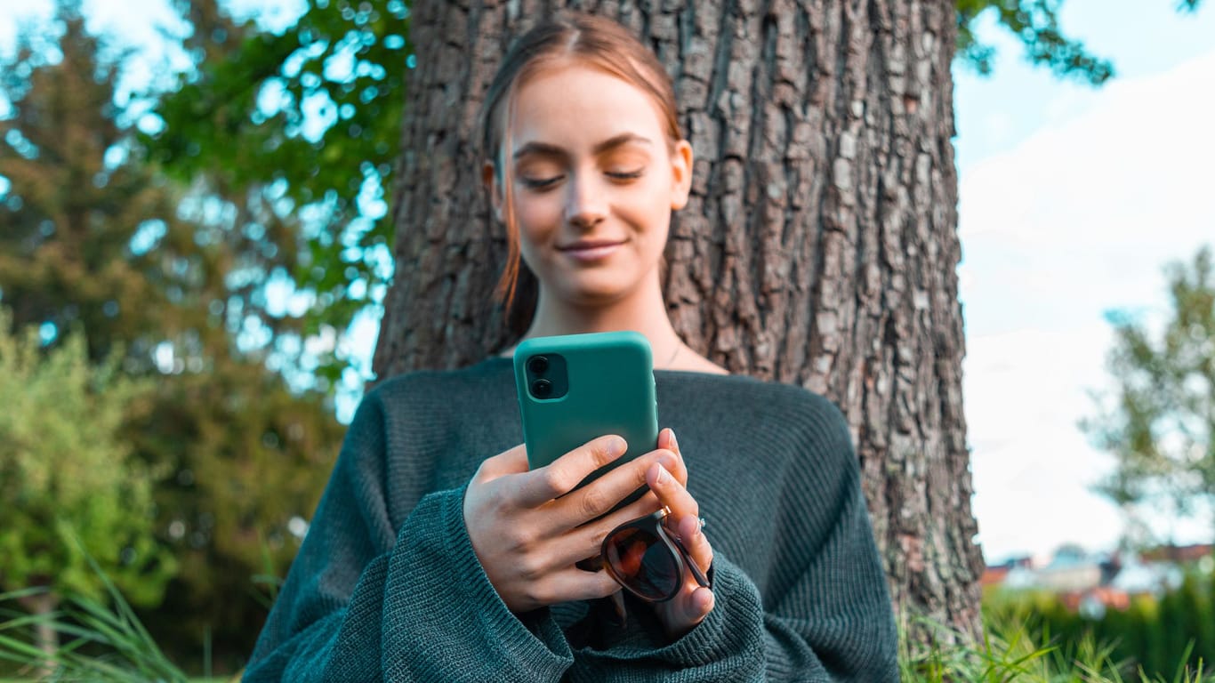Frau blickt lächelnd auf ihr Smartphone (Symbolbild): Der Online-Händler Amazon plant angeblich den Einstieg in den Mobilfunk-Markt.