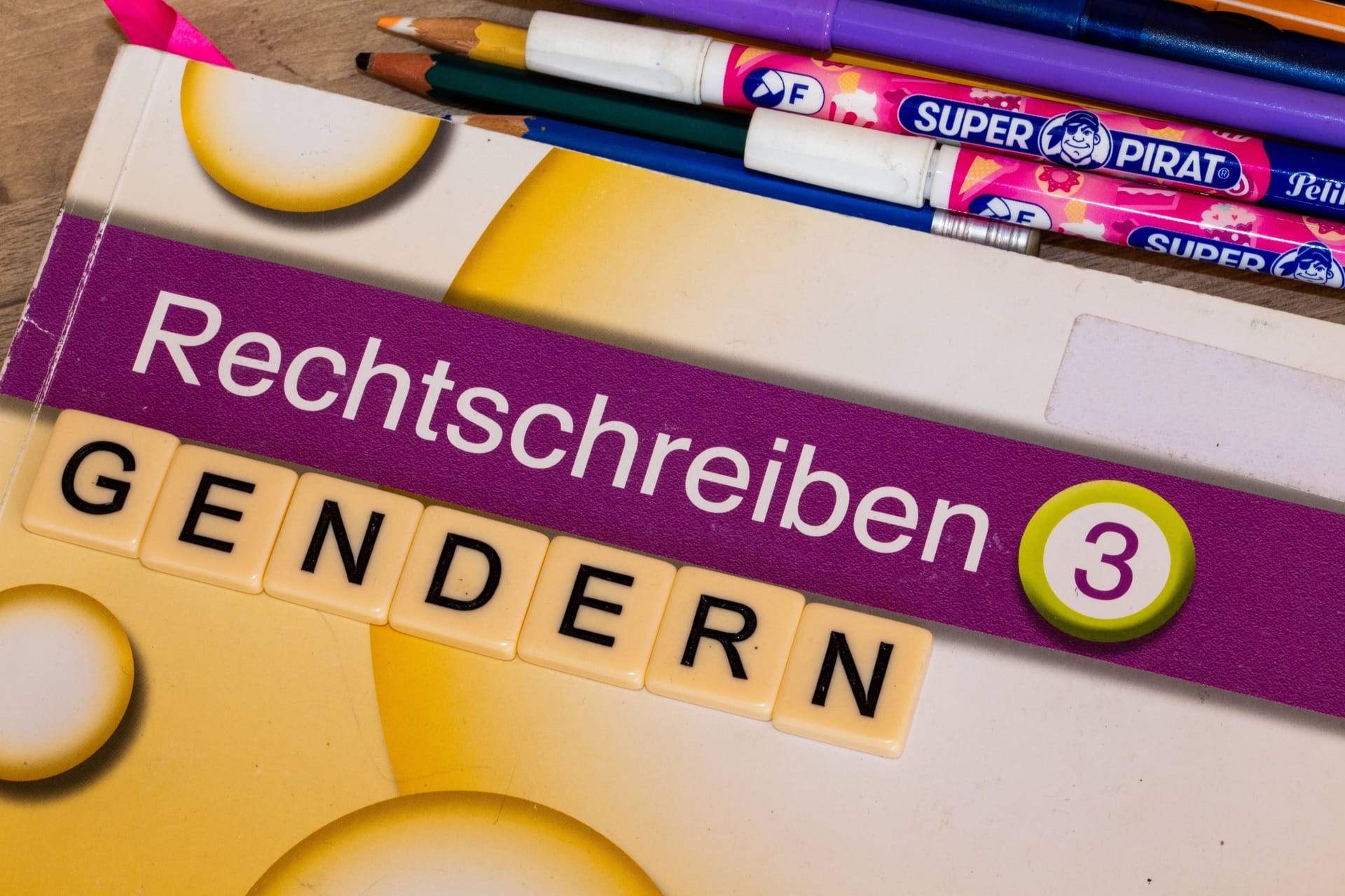 Buchstabenwürfel auf einem Grundschulbuch zeigen das Wort Gendern (Symbolbild): Sachsen verbannt das Gendersternchen endgültig aus den Klassenzimmern.