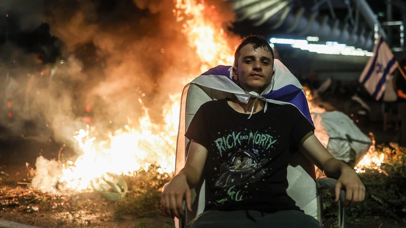 Ein israelischer Demonstrant sitzt vor einem Feuer auf den Straßen Tel Avivs: Die Proteste gegen die Selbstermächtigung der israelischen Regierung brechen nicht ab.