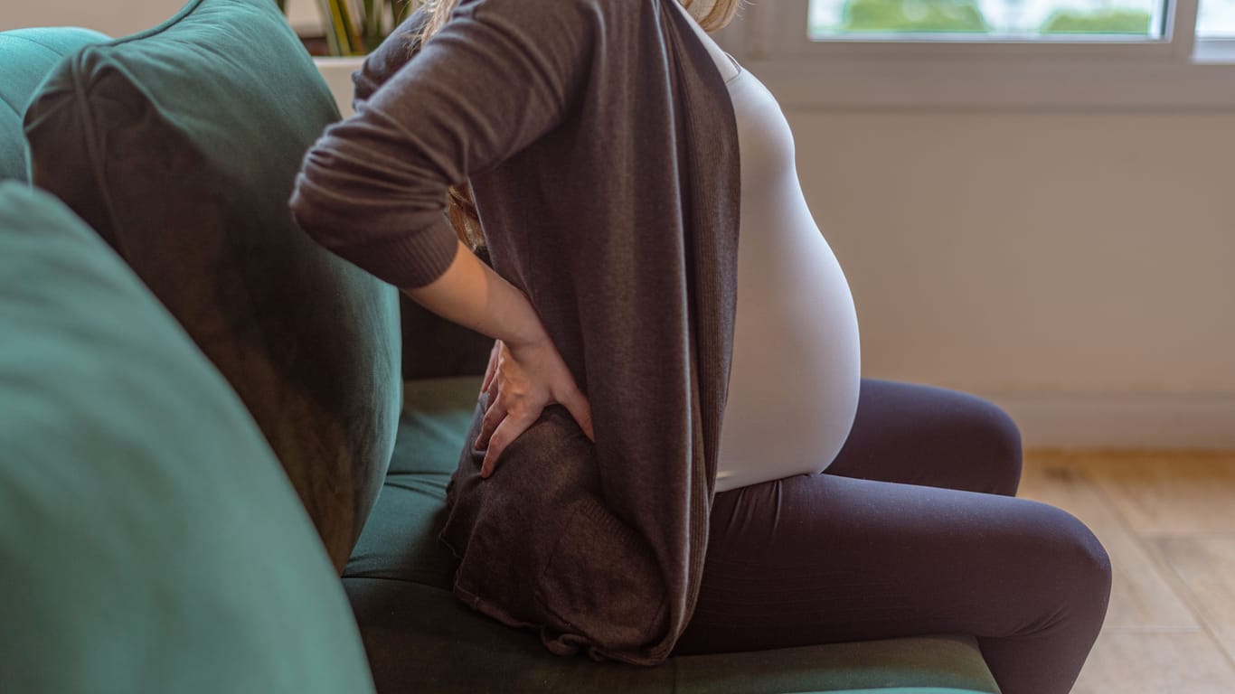 Schwangere Frau auf Sofa: Schreitet die Schwangerschaft voran, können sich Steißbeinschmerzen einstellen.