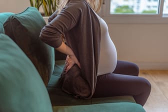 Schwangere Frau auf Sofa: Schreitet die Schwangerschaft voran, können sich Steißbeinschmerzen einstellen.