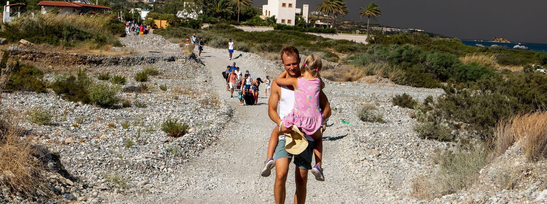 Rhodos: Ein Mann trägt ein Kind, als sie ein Gebiet verlassen, in dem ein Waldbrand wütet.