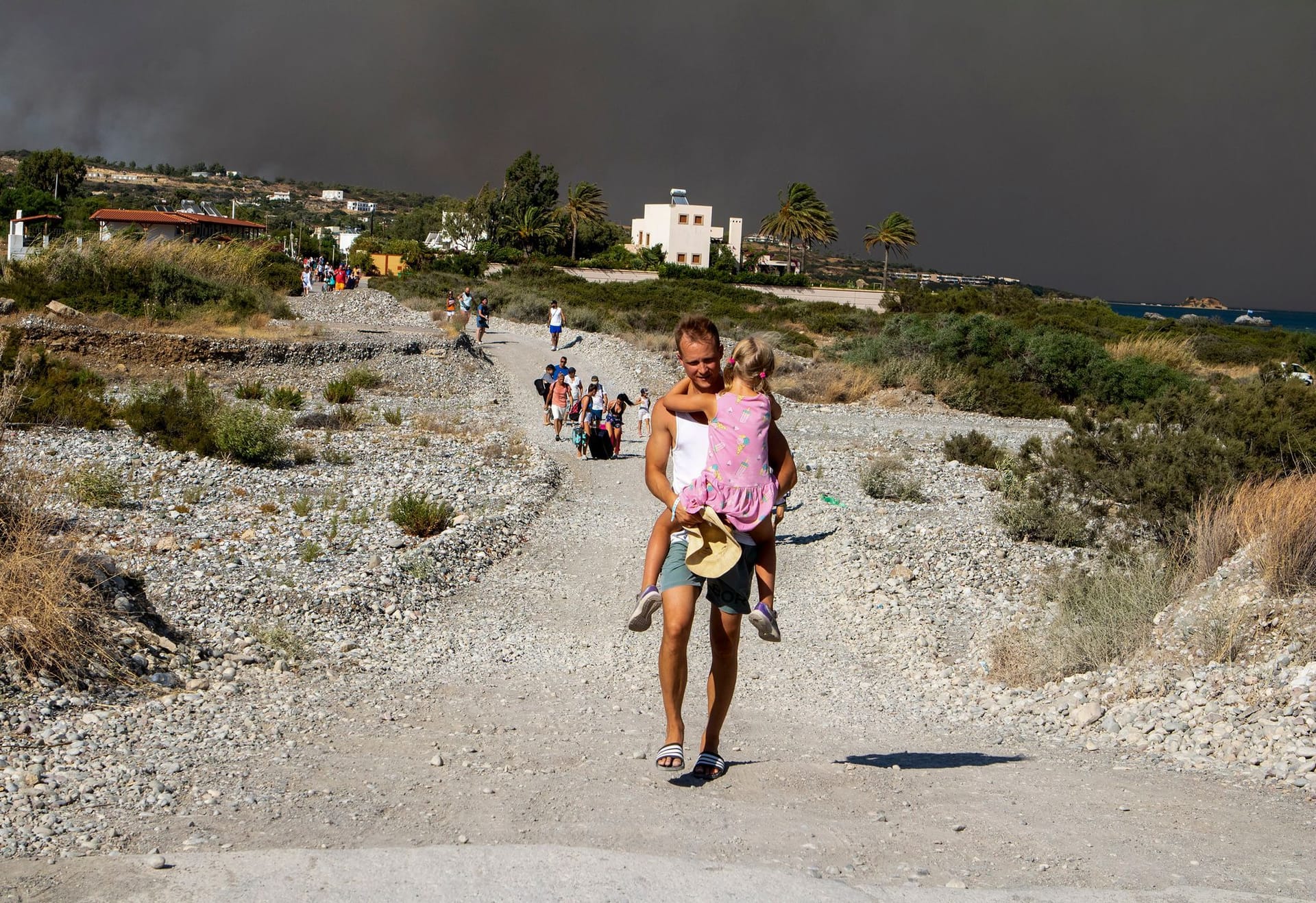 Rhodos: Ein Mann trägt ein Kind, als sie ein Gebiet verlassen, in dem ein Waldbrand wütet.