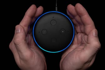 Person using an illuminated Amazon Echo Dot smart speaker.