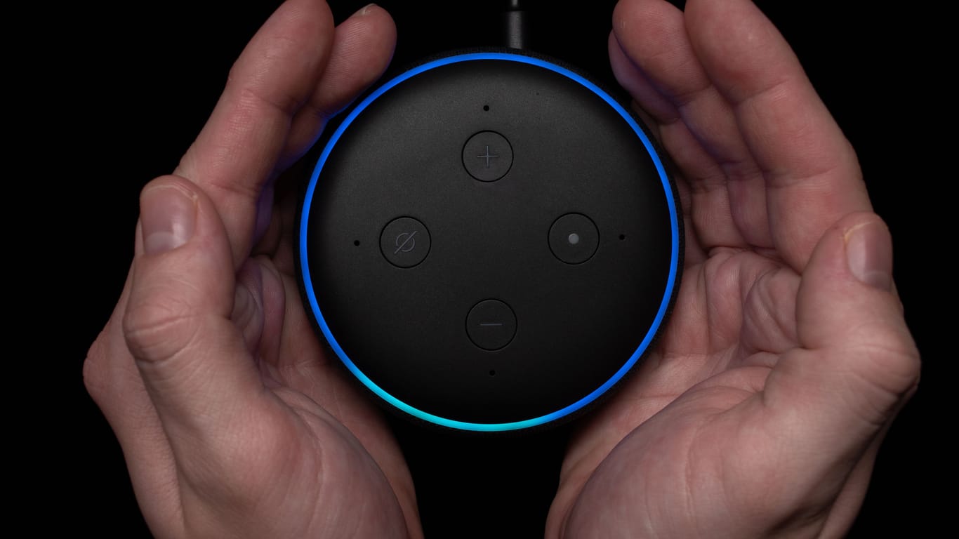 Person using an illuminated Amazon Echo Dot smart speaker.