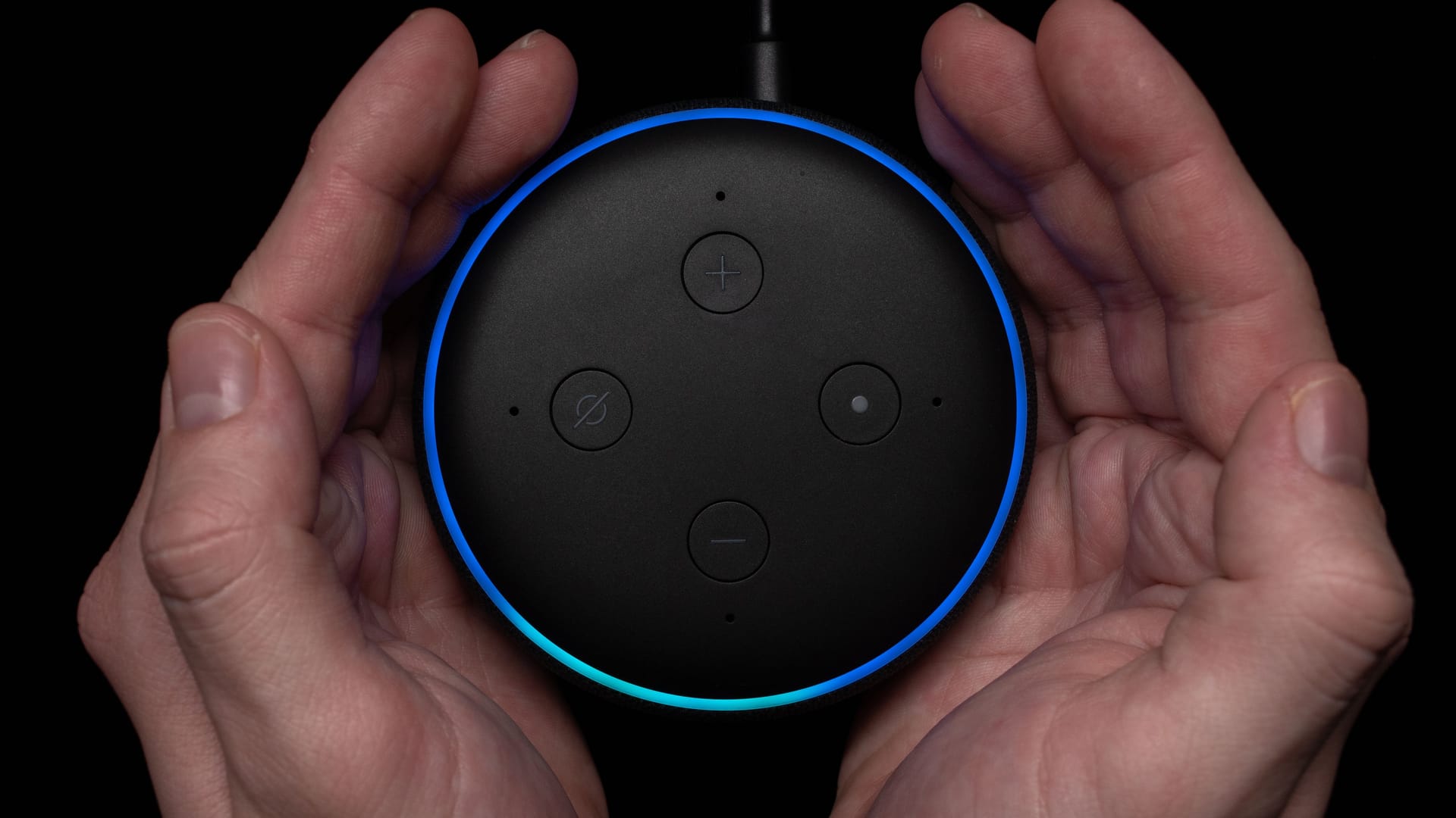 Person using an illuminated Amazon Echo Dot smart speaker.