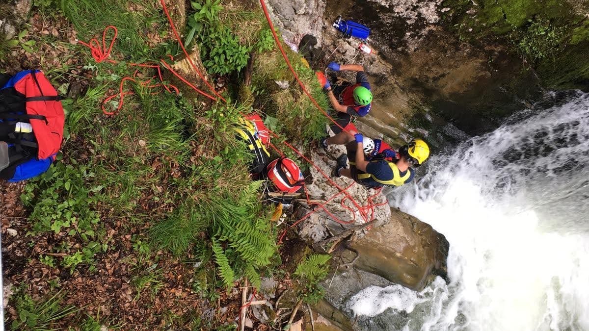 Einsatz an einer Felswand in den Bergen (Archivbild): Mehrere Kräfte der Bergwand hängen über tosendem Wasser an Seilen.