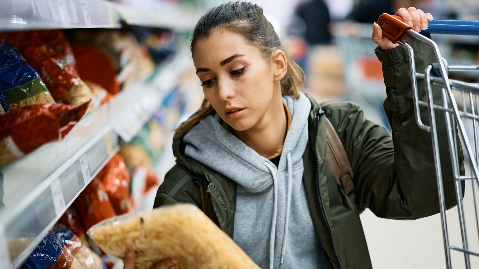 Frau im Supermarkt betrachtet eine Packung Nudeln