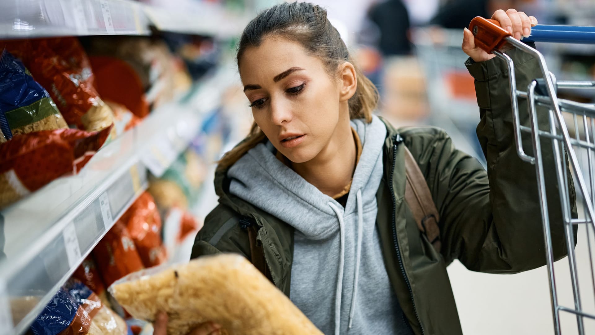 Frau im Supermarkt betrachtet eine Packung Nudeln Frau im Supermarkt betrachtet eine Packung Nudeln