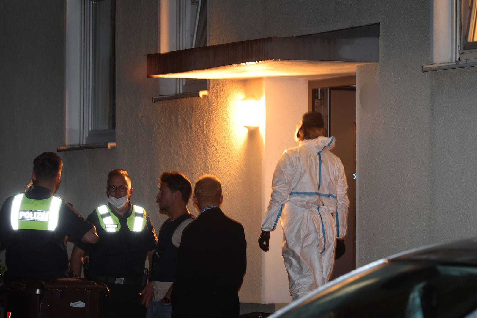 Polizisten und ein Beamter der Spurensicherung stehen vor einem Haus, in dem drei Menschen erschossen wurden