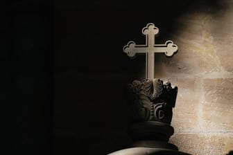 Ein Lichtstrahl fällt in einer Kirche auf ein Kreuz (Symbolbild): Katholische Kirche entlässt Priester aus Klerikerstand.
