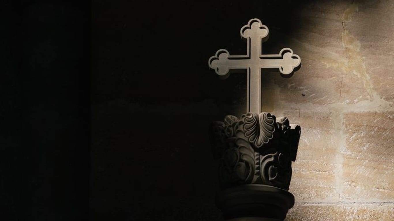 Ein Lichtstrahl fällt in einer Kirche auf ein Kreuz (Symbolbild): Katholische Kirche entlässt Priester aus Klerikerstand.