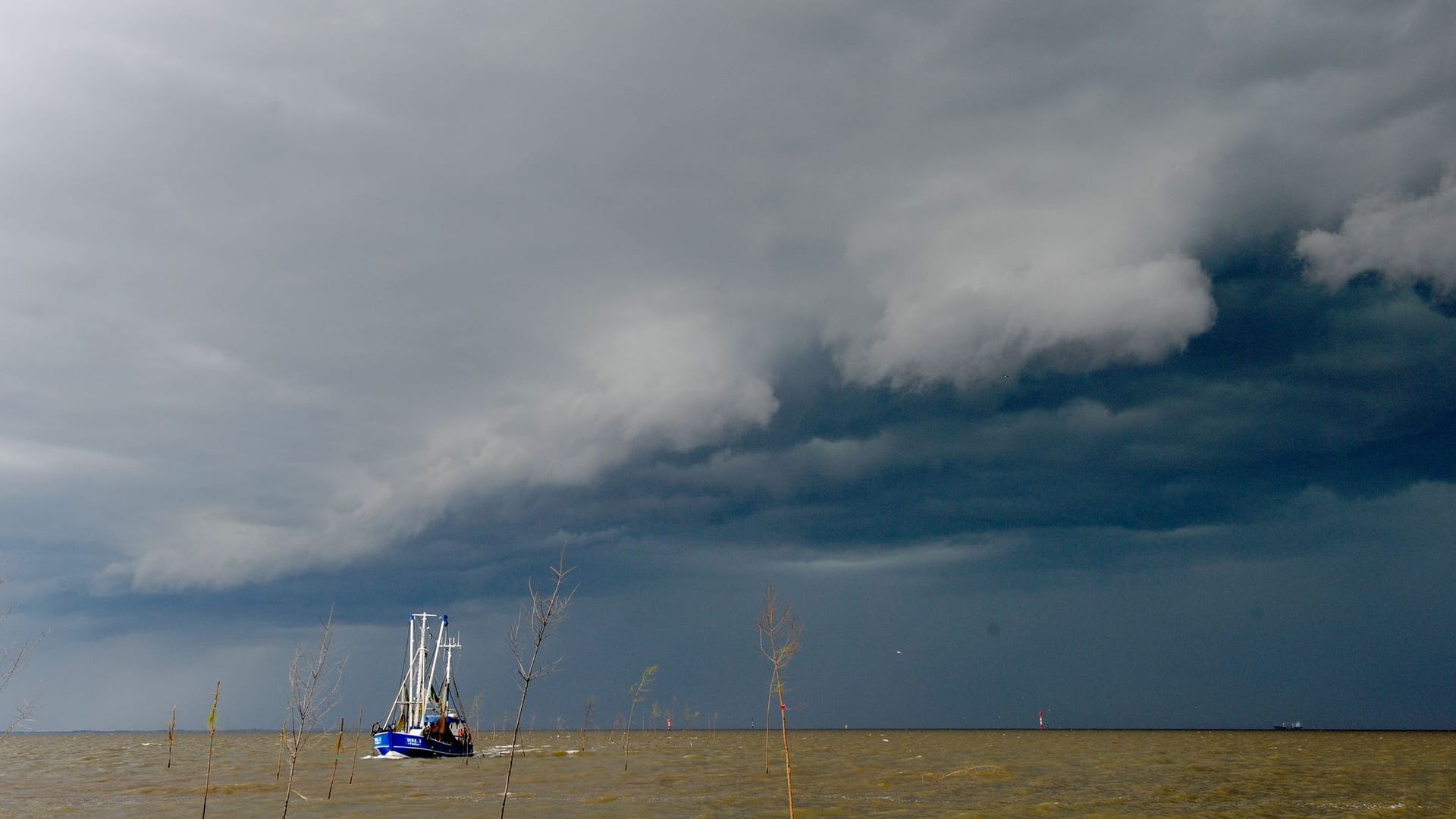 Gewitterfront an der Nordseeküste (Symbolbild): Ein Krabbenkutter kehrt vor einem heraufziehenden Gewitter in den schützenden Hafen zurück.