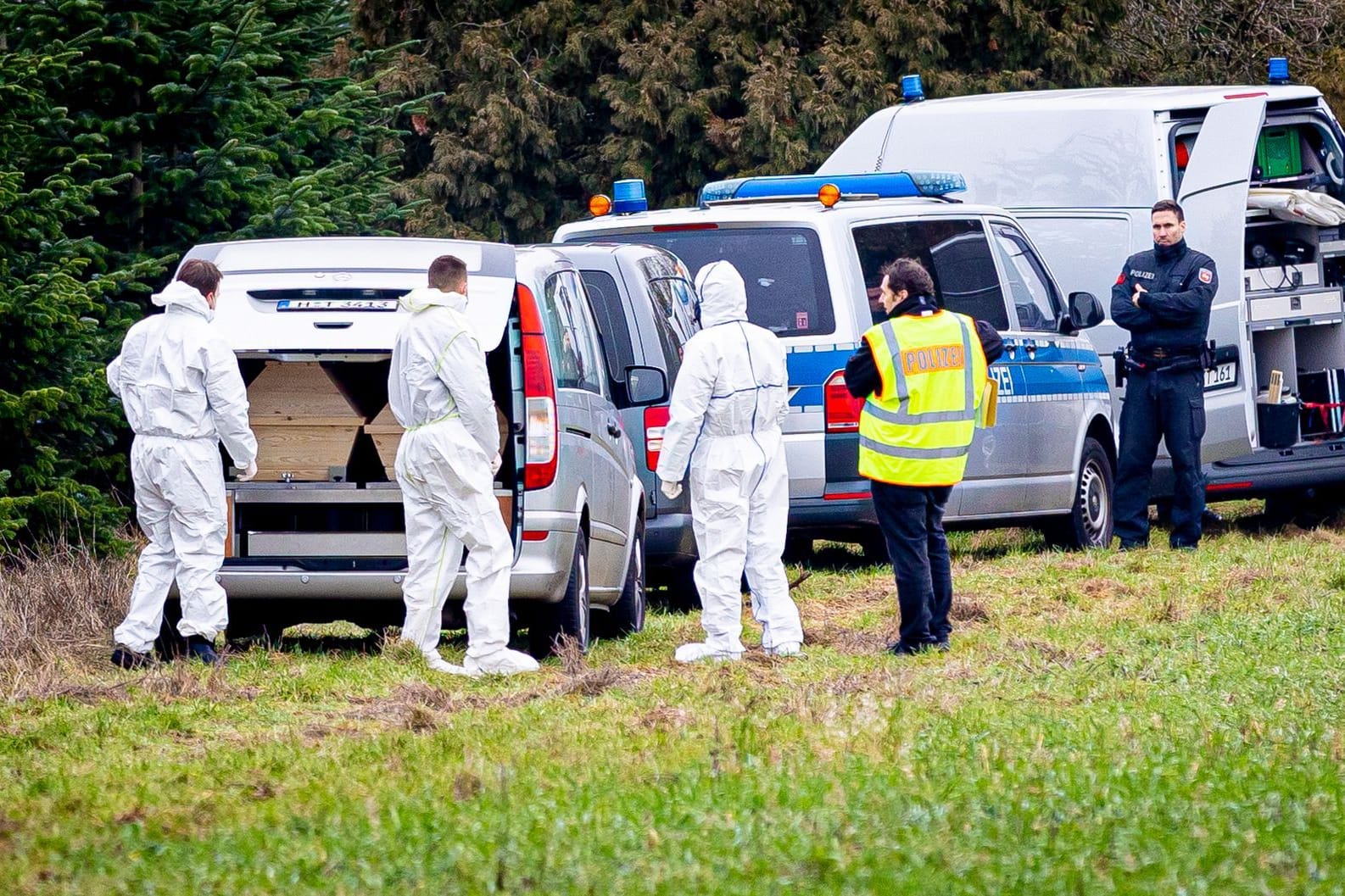 Mitarbeiter der Spurensicherung der Polizei stehen an einem Leichenwagen, der auf einer Wiese in Wunstorf parkt (Archivbild): In der Nähe wurde im Januar die Leiche eines 14-Jährigen gefunden.