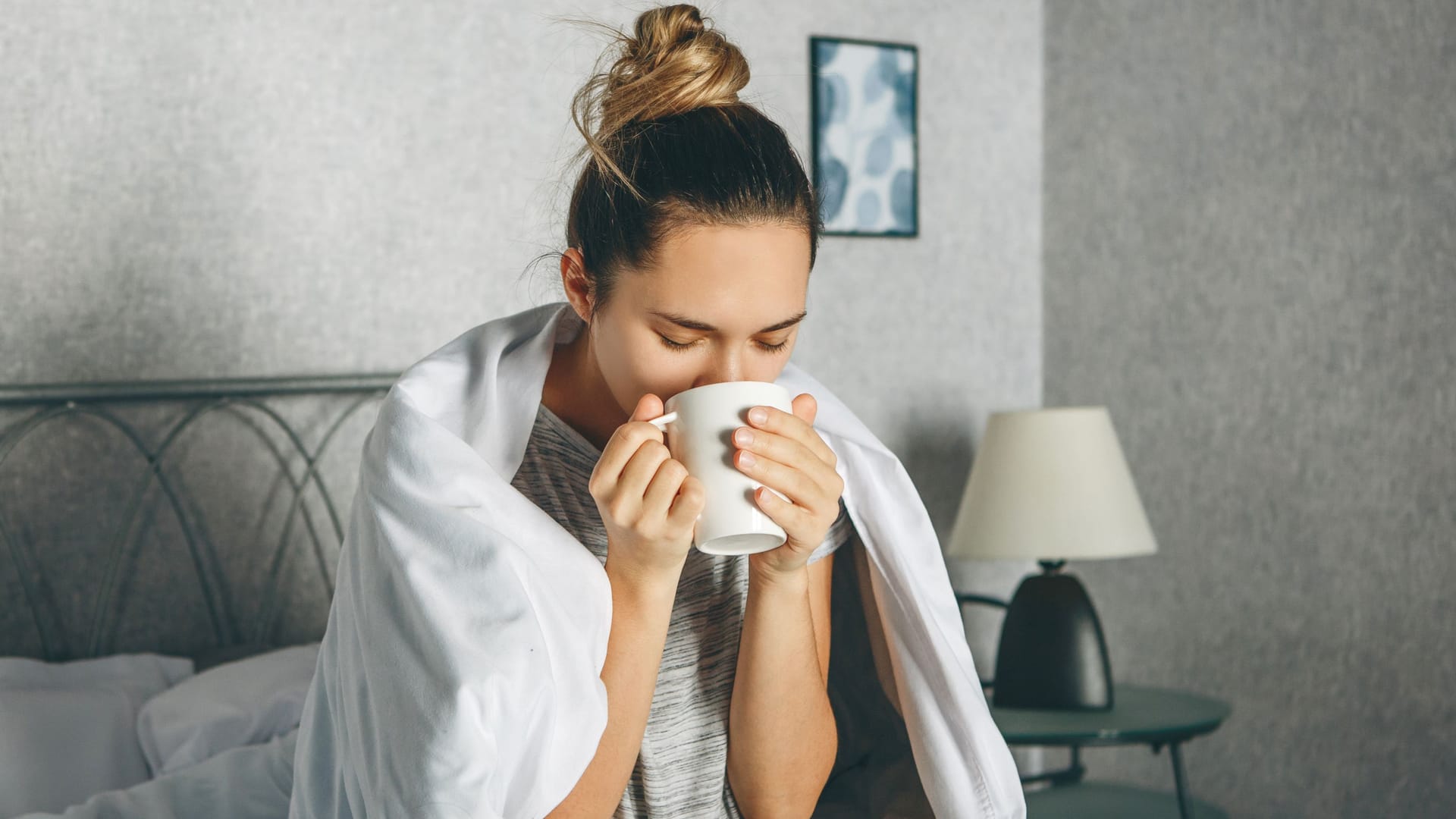 Frau sitzt im Bett und trinkt aus einer Tasse Frau sitzt im Bett und trinkt aus einer Tasse