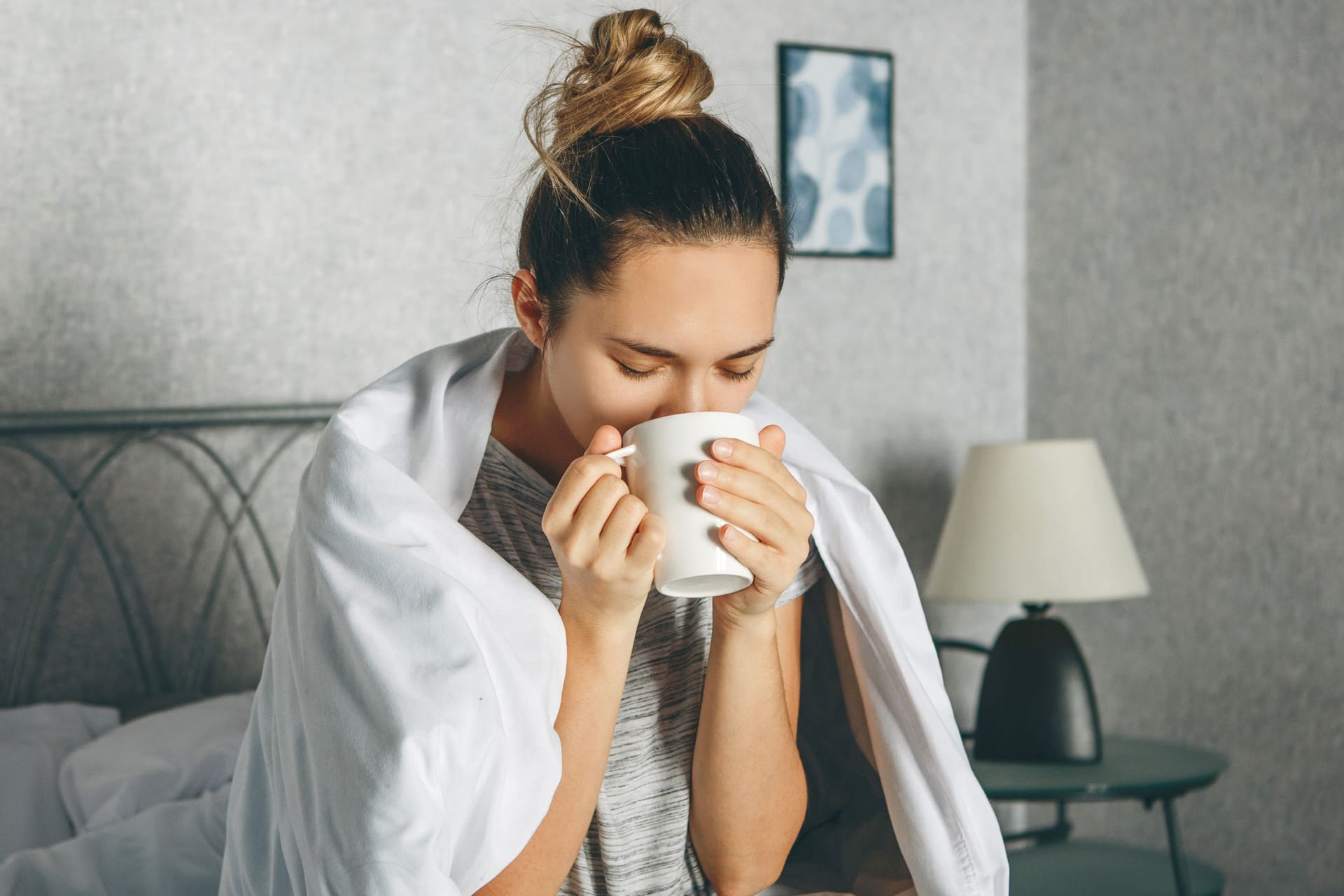 Frau sitzt im Bett und trinkt aus einer Tasse