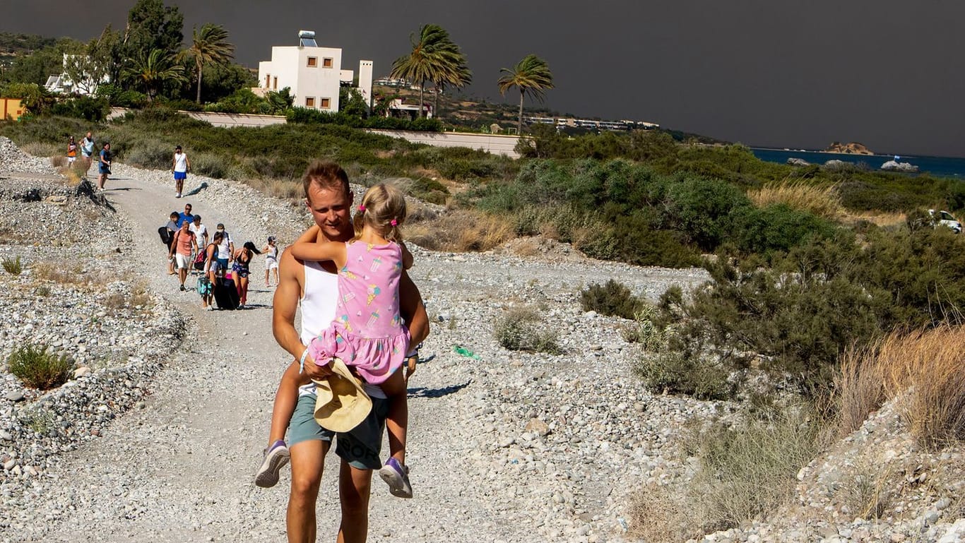 Ein Mann trägt ein Kind, als sie ein Gebiet verlassen, in dem ein Waldbrand auf der griechischen Insel Rhodos wütet.