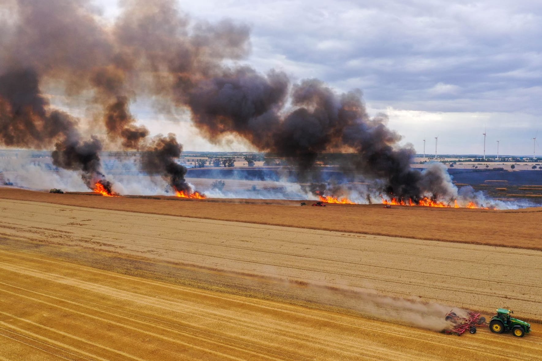 Mit einem Traktor pflügt ein Landwirt einen Schutzstreifen: Das Getreidefeld steht in Flammen.
