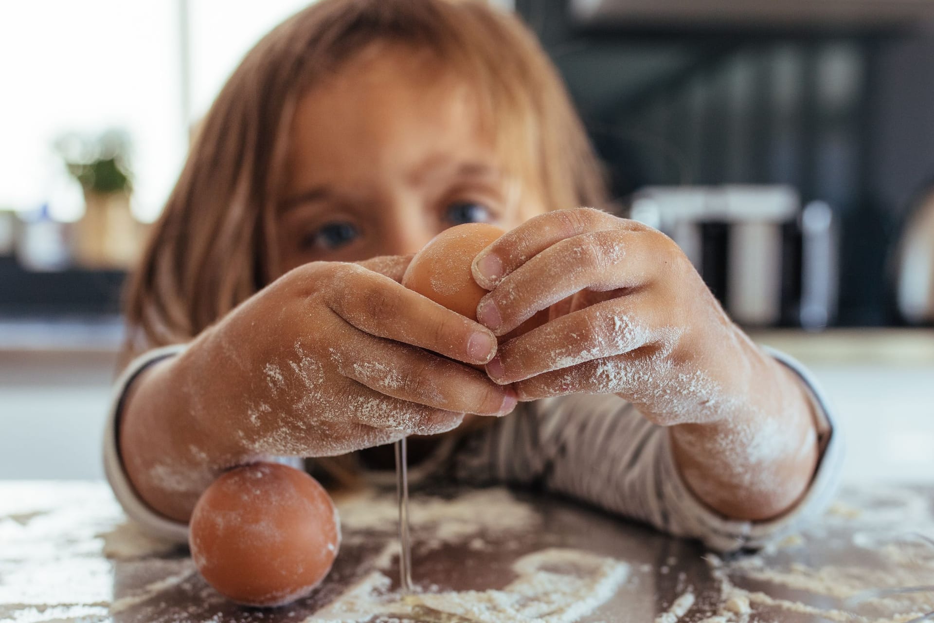 Kind schlägt ein Ei über bemehlter Küchenarbeitsfläche auf