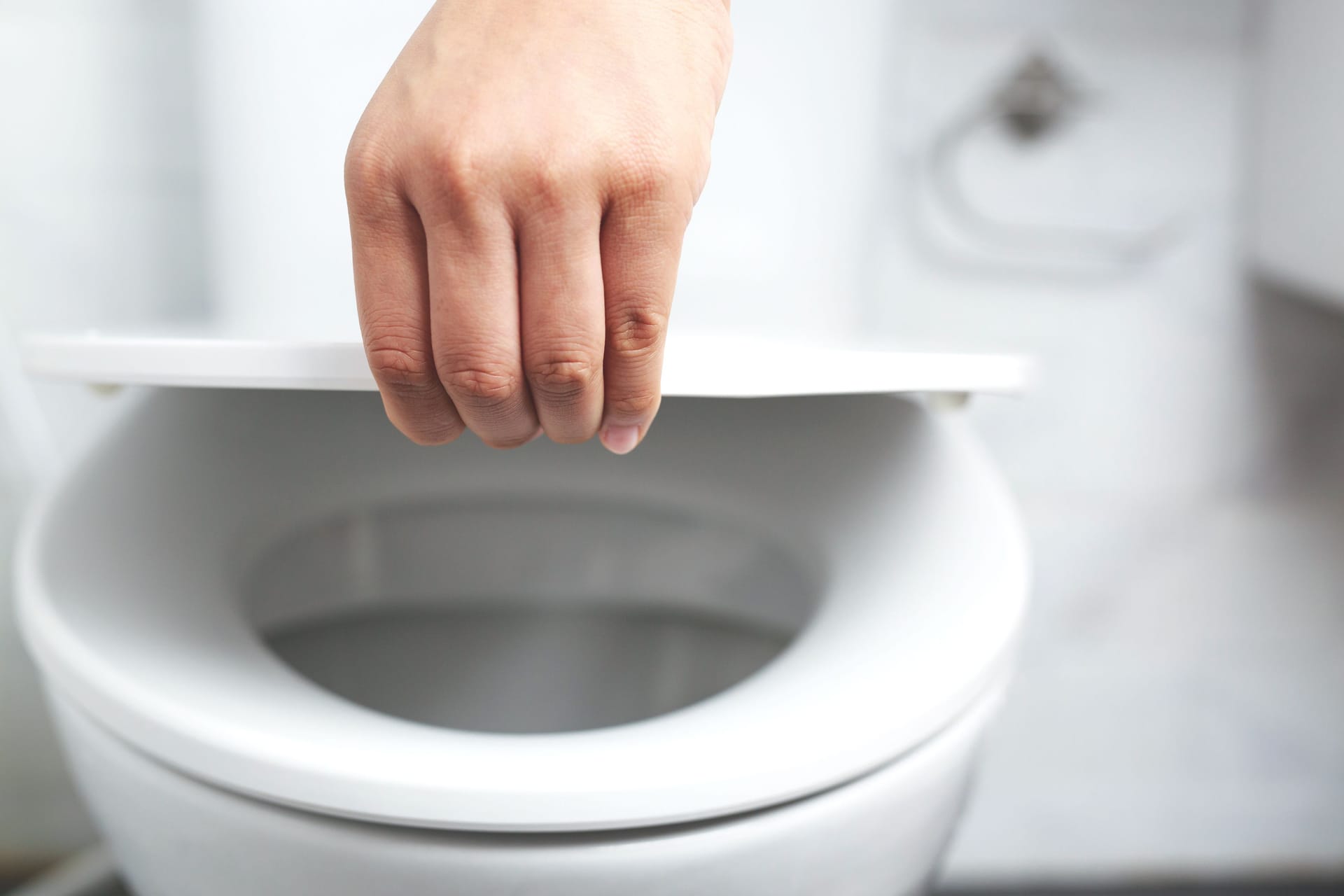Jemand hebt den Deckel einer Toilette an Jemand hebt den Deckel einer Toilette an