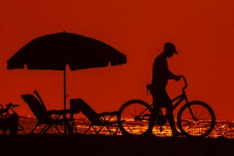 Ein Mann schiebt sein Fahrrad durch die Abenddämmerung eines besonders heißen Tages an der Küste von South Carolina: Weltweit macht ein besonders heißer Juli den Menschen zu schaffen.