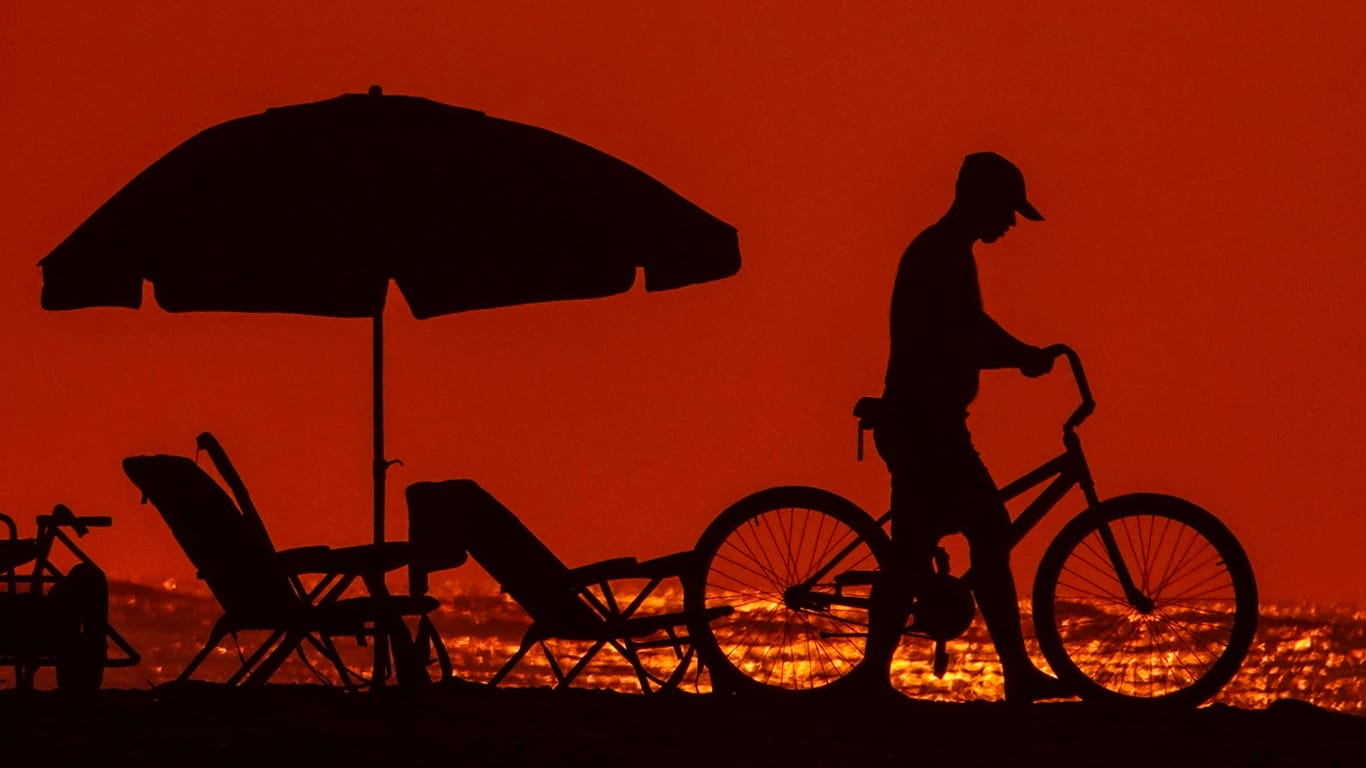 Ein Mann schiebt sein Fahrrad durch die Abenddämmerung eines besonders heißen Tages an der Küste von South Carolina: Weltweit macht ein besonders heißer Juli den Menschen zu schaffen.