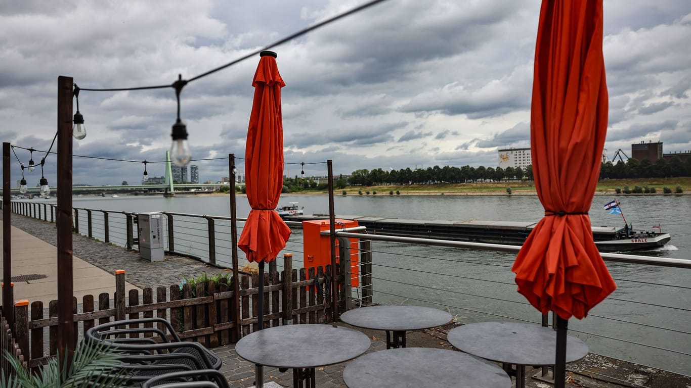 Köln: Graue Wolken bedecken den Himmel über einem Café am Rheinufer.