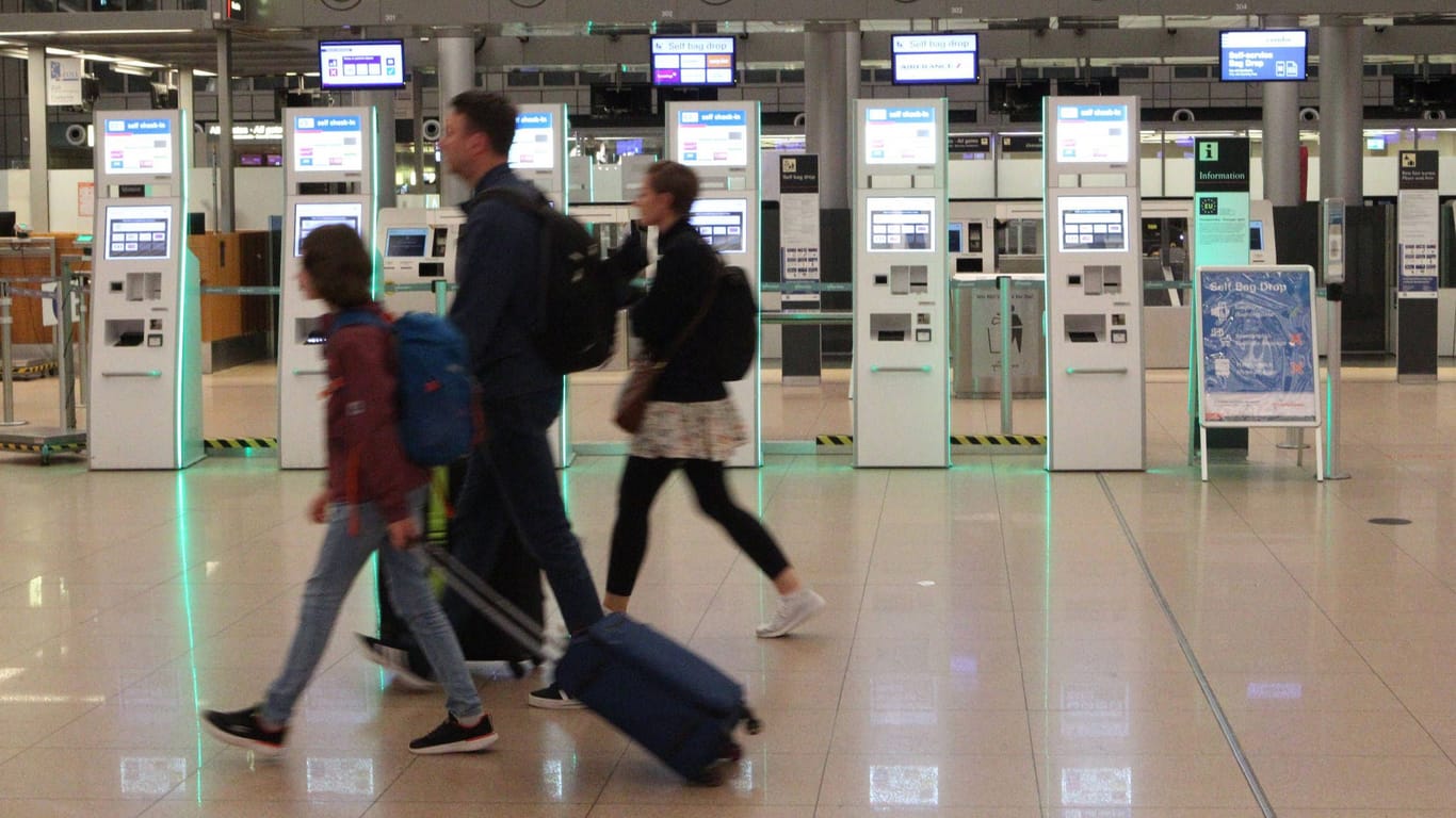 Eine Familie geht durchs Terminal 2 vom Flughafen Hamburg (Archivbild): Im Hintergrund sind Automaten zum Selbsteinchecken und für die Gepäckaufgabe zu sehen.