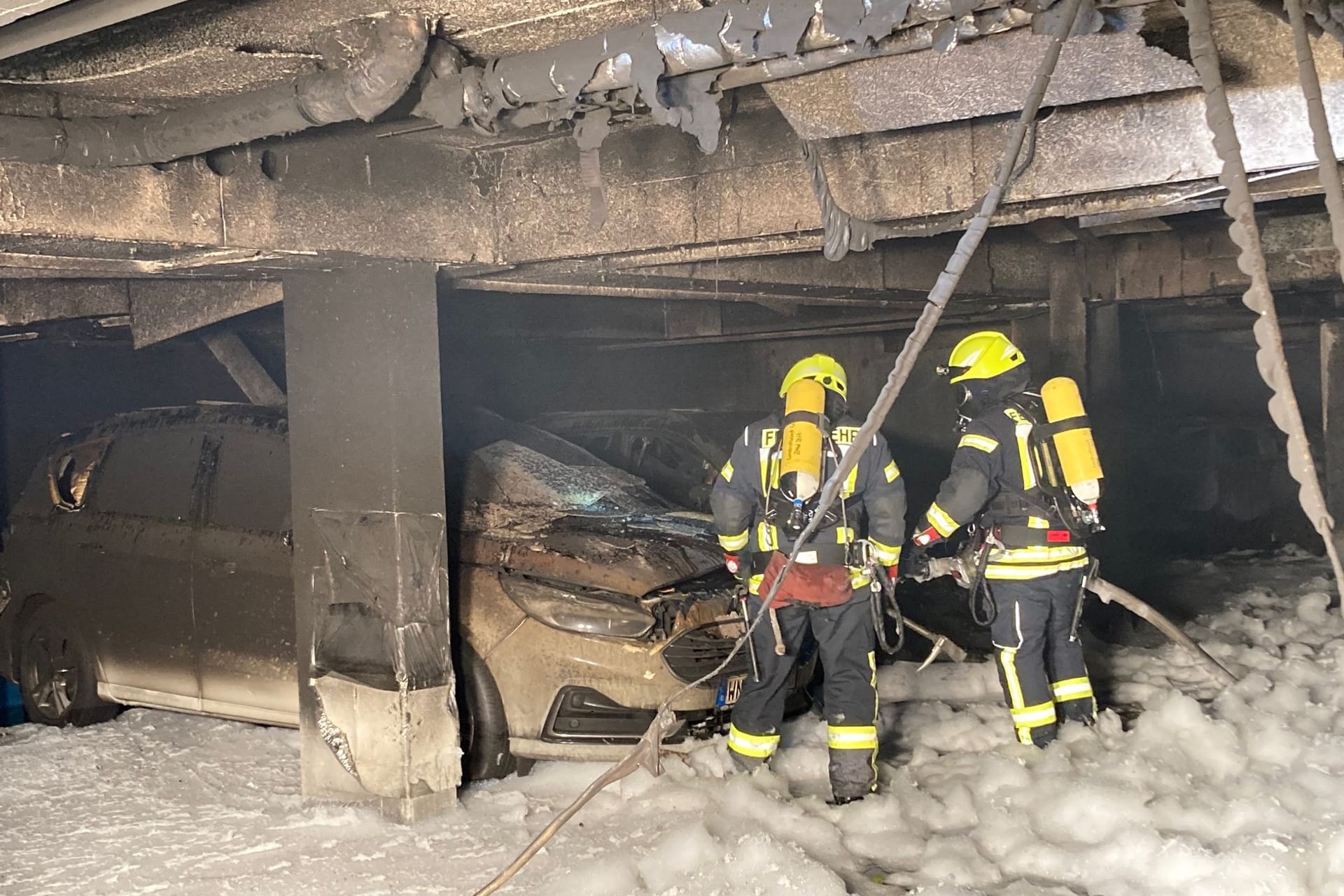 Zwei Feuerwehrleute stehen nach dem Brand in der Tiefgarage: Aus bislang unbekannter Ursache war ein Auto in Brand geraten.