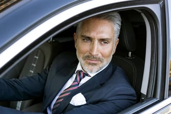 Ein erfolgreicher Geschäftsmann sitzt in einem schicken Auto (Symbolbild): Gutverdiener werden geringwertschätzt, kritisieren manche.