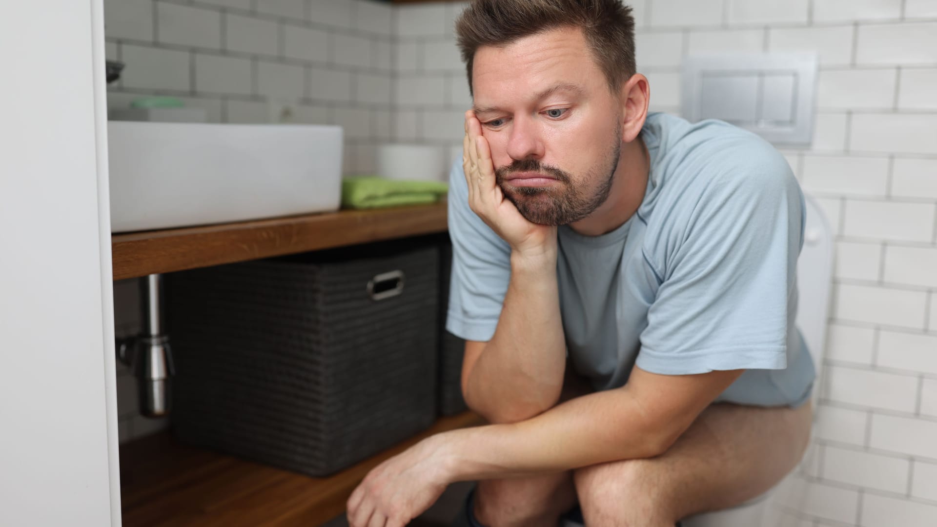 Mann sitzt nachdenklich auf der Toilette