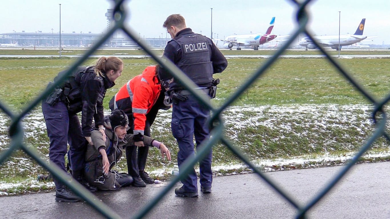 Brandenburg, Schönefeld: Zwei Beamte der Bundespolizei und ein Sicherheitsmitarbeiter stehen mit einem Aktivisten der "Letzten Generation" an einem Zaun am BER-Flughafen.