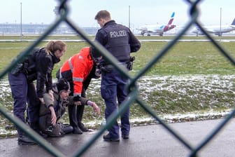Brandenburg, Schönefeld: Zwei Beamte der Bundespolizei und ein Sicherheitsmitarbeiter stehen mit einem Aktivisten der "Letzten Generation" an einem Zaun am BER-Flughafen.