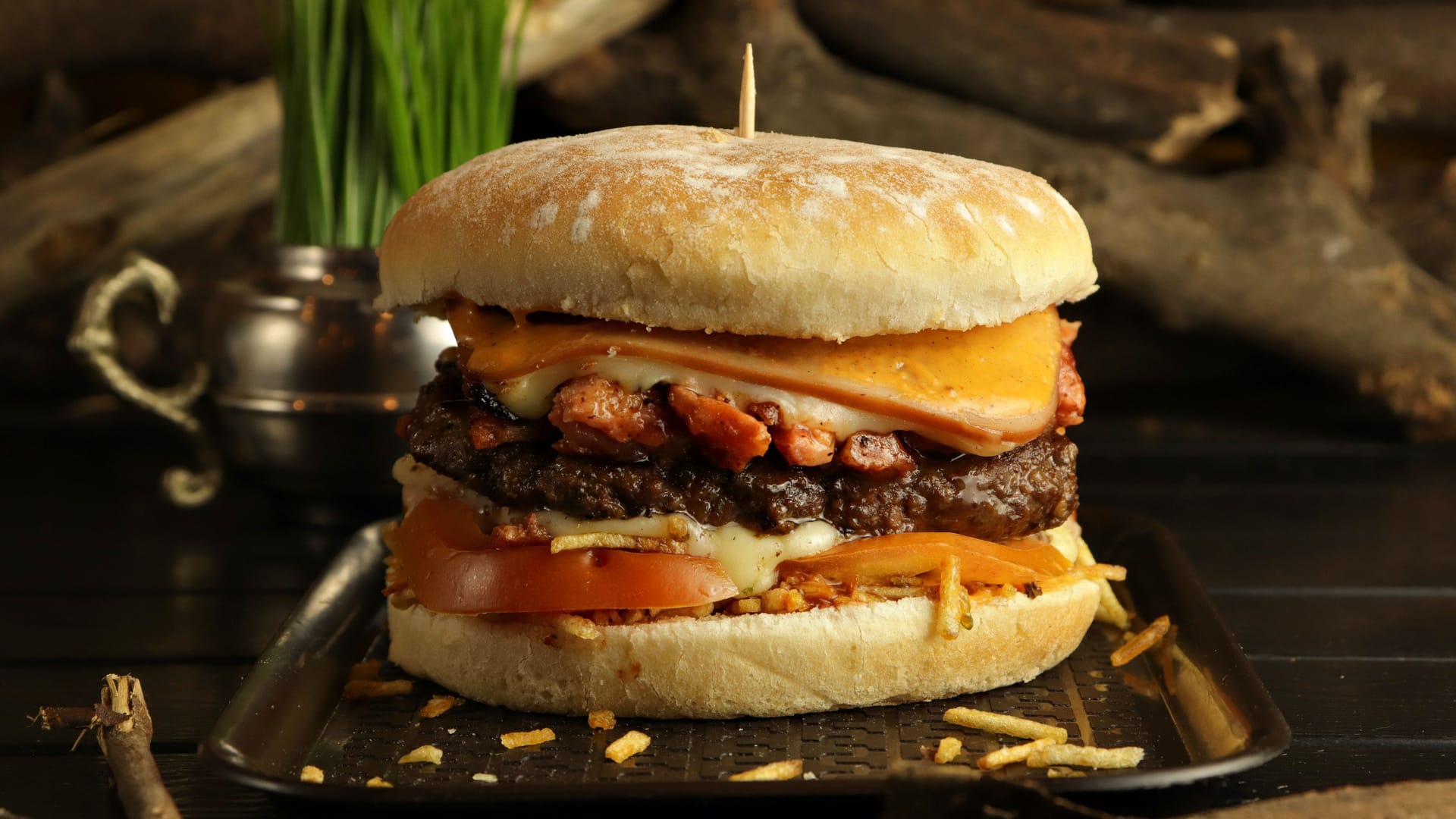 Closeup of a delicious burger with beef, melted cheese, chips, and tomatoes on a tray