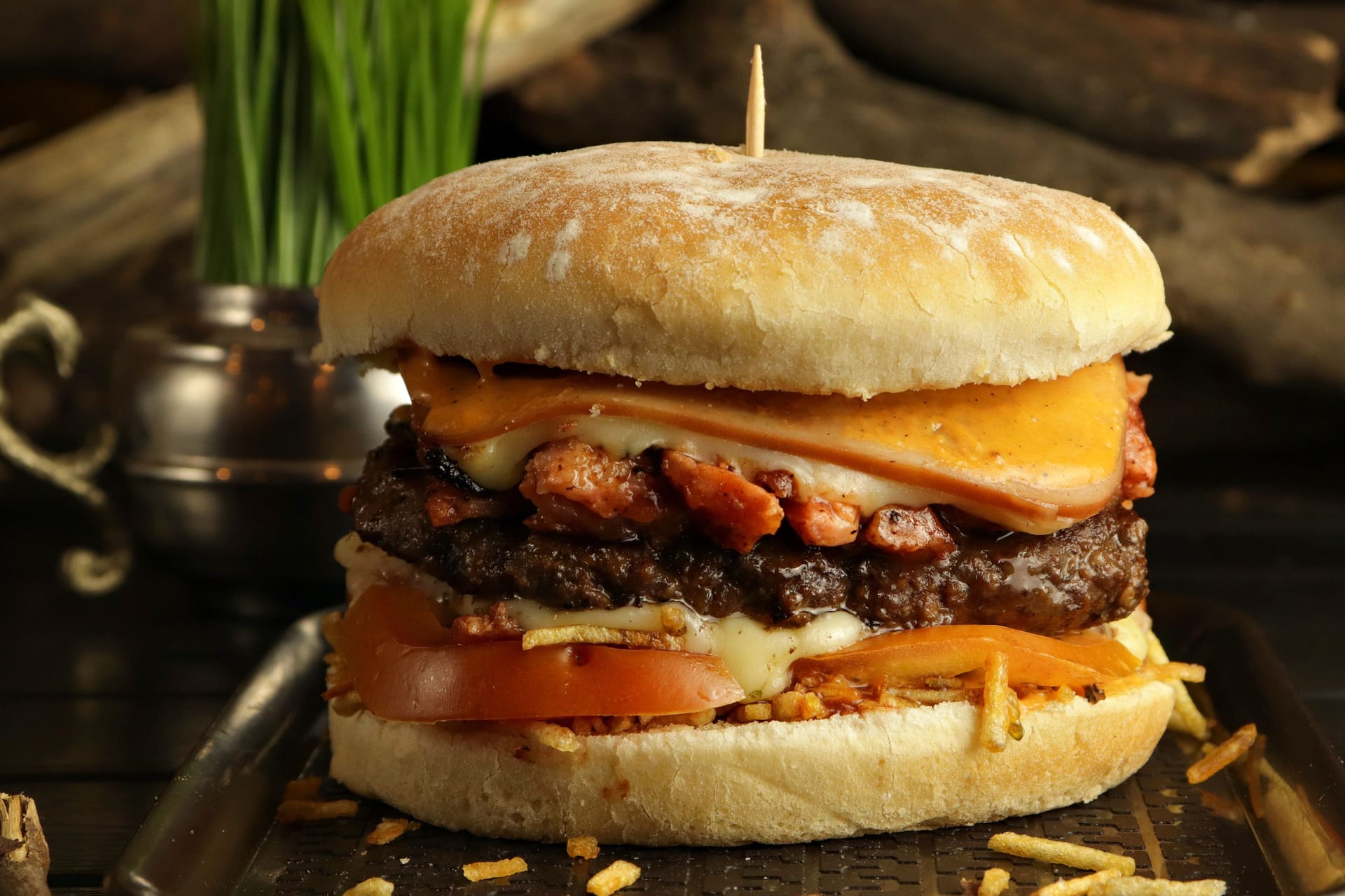 Closeup of a delicious burger with beef, melted cheese, chips, and tomatoes on a tray